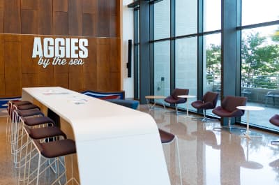 Waiting area with large white tabletop seating and Aggies by the Sea sign. Texas A&M University at Galveston in Galveston, Texas, on July 28, 2022. (Laura McKenzie/Texas A&M University Division of Marketing & Communications)
