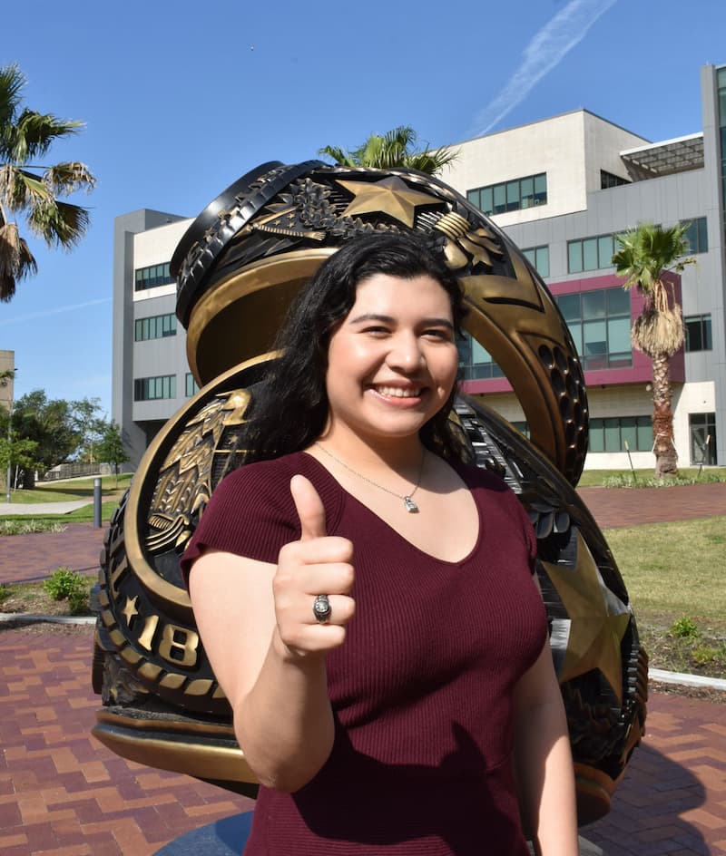 Student Gema Garcia '24 posing in front of the Aggie Ring Statue at the Galveston campus